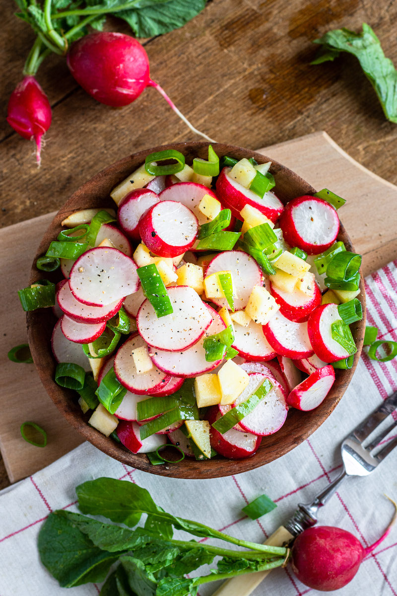 Salat mit Radieschen, Apfel und Frühlingszwiebeln in einer Holzschüssel serviert