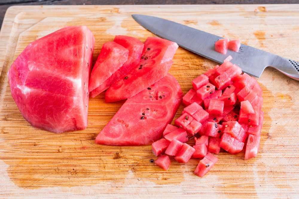 Geschälte Wassermelone wird auf einem Schneidbrett in kleine Würfel geschnitten.