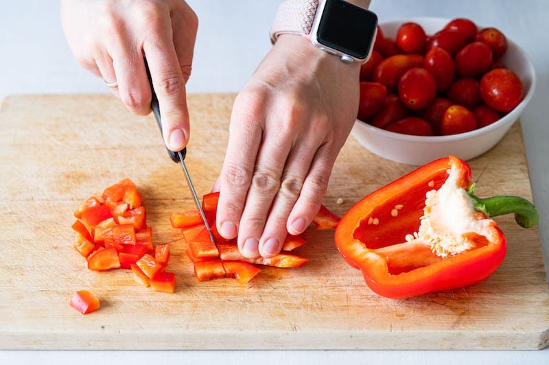 Eine rote Paprika wird auf einem Schneidbrett in kleine Würfel geschnitten.